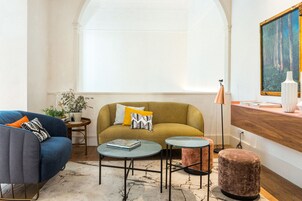 Una sala de estar con sofá, sillón, mesa de centro, reposapiés y un cuadro en la pared.