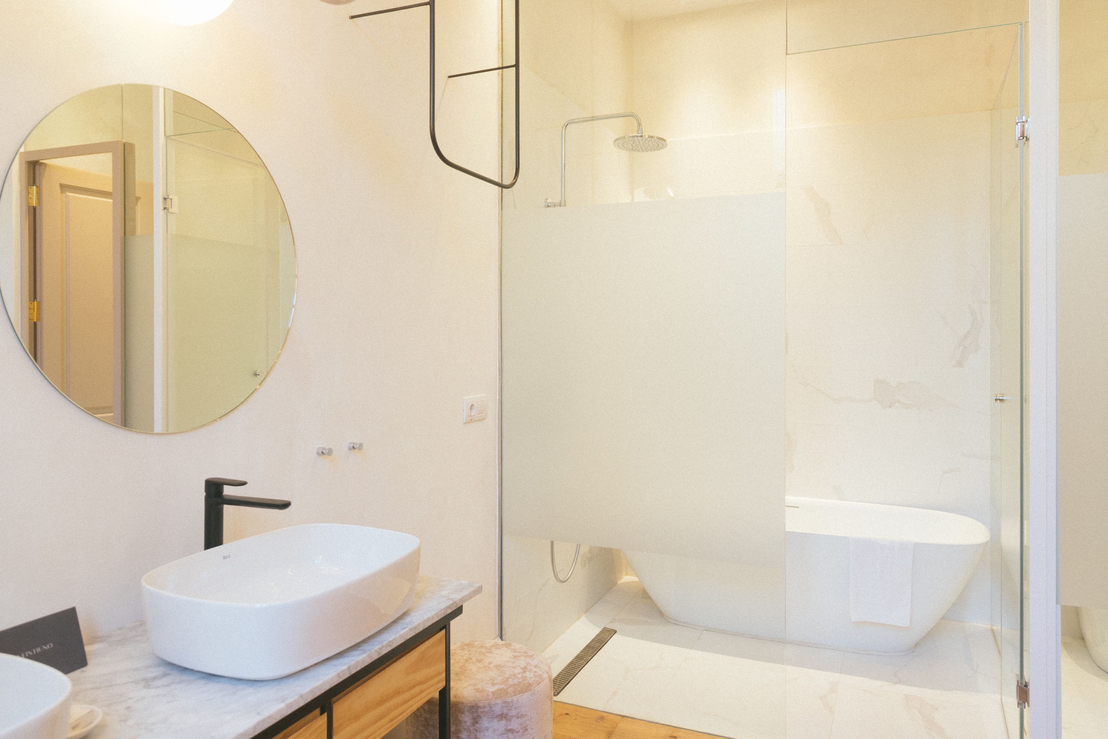 A modern bathroom with a large round mirror, a white sink, and a freestanding bathtub.