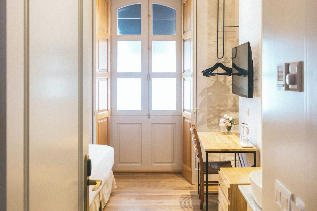 A narrow hallway with a wooden floor, a ceiling fan, and a double door with glass panels.
