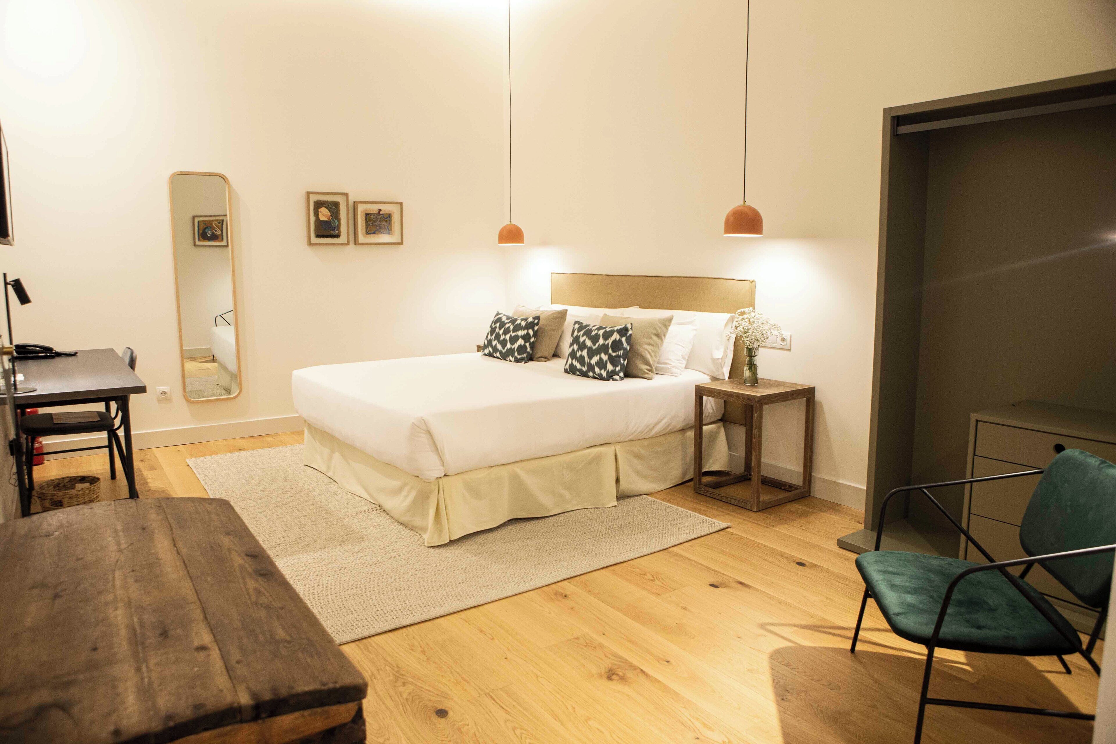 Une chambre à coucher comprenant un lit, une table de chevet, une chaise, un plancher en bois et un miroir.