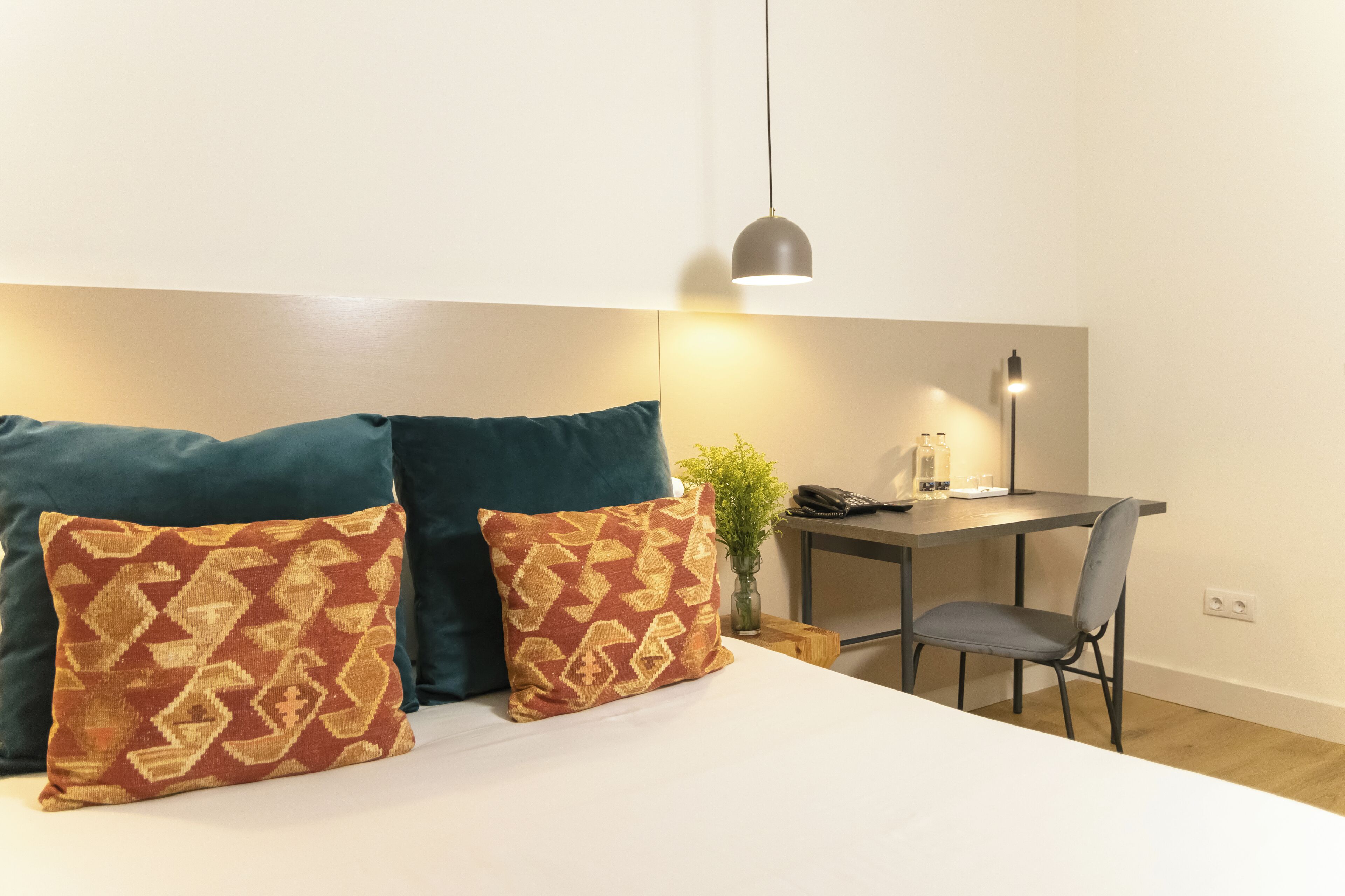 Un dormitorio con cama, dos almohadas, escritorio, silla y lámpara colgante.