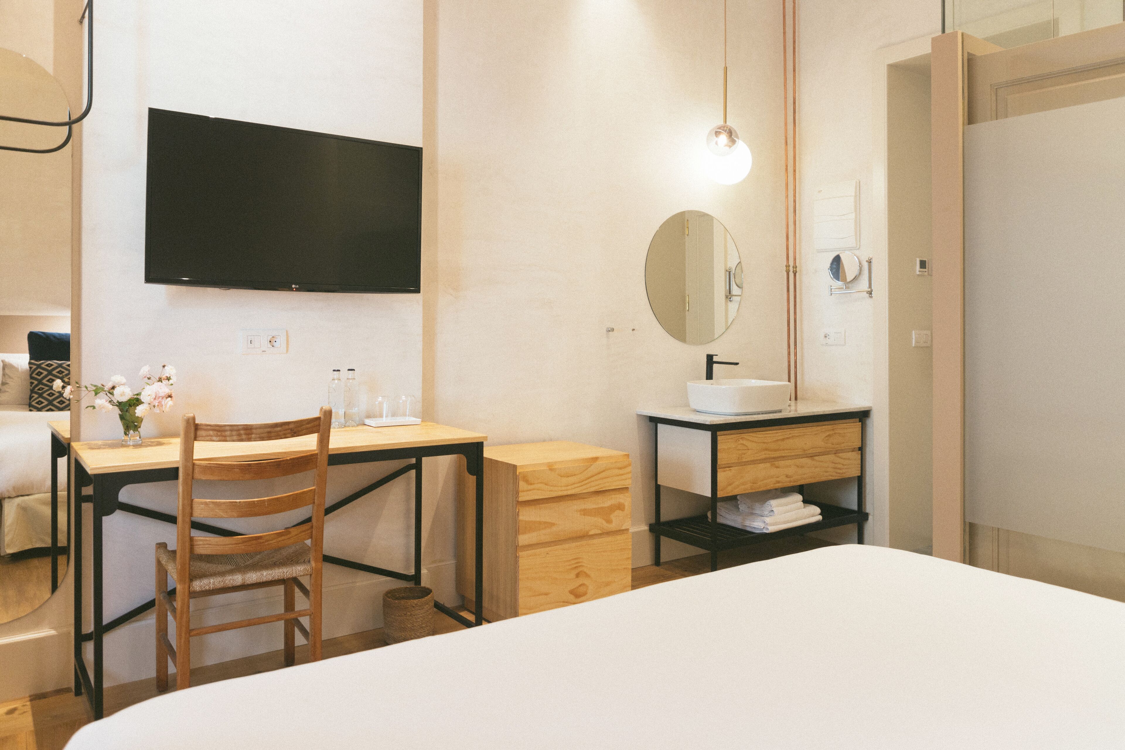 Een hotelkamer met een bed, een bureau met stoel, een televisie, een wastafel en een spiegel.