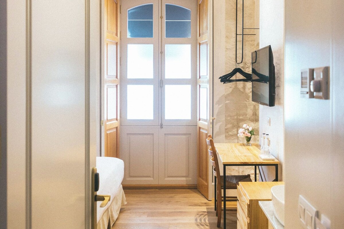 Un couloir étroit doté d’un plancher en bois, d’un ventilateur de plafond et d’une porte avec des panneaux en verre dépoli.