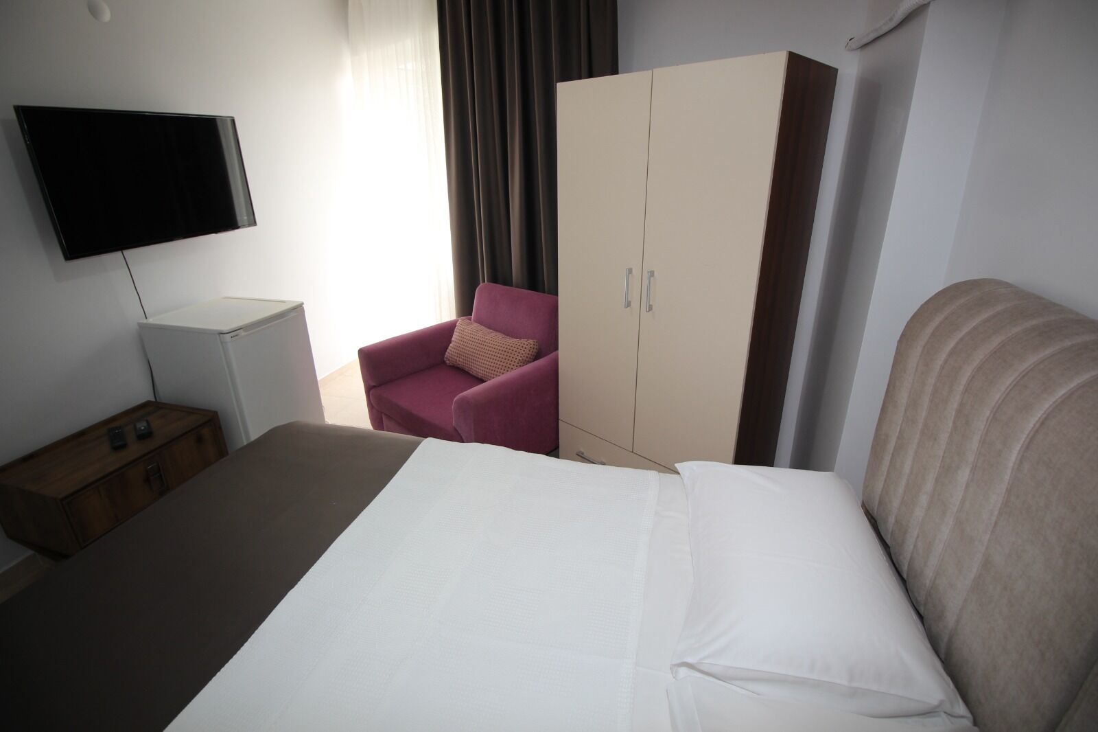 A hotel room with a bed, a TV, a wardrobe, a chair, and a bedside table.