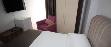 A hotel room with a bed, a TV, a wardrobe, a chair, and a bedside table.