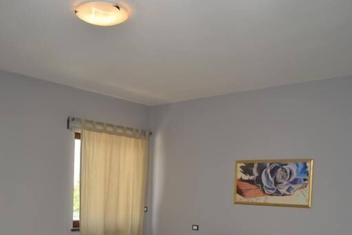 A bedroom with a bed, a painting on the wall, and a window with curtains.