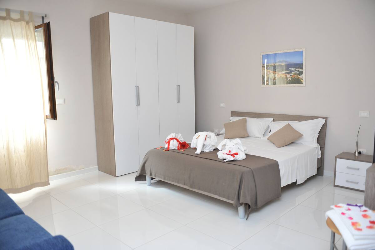 A bedroom with a large wardrobe, a bed with pillows, and a nightstand.