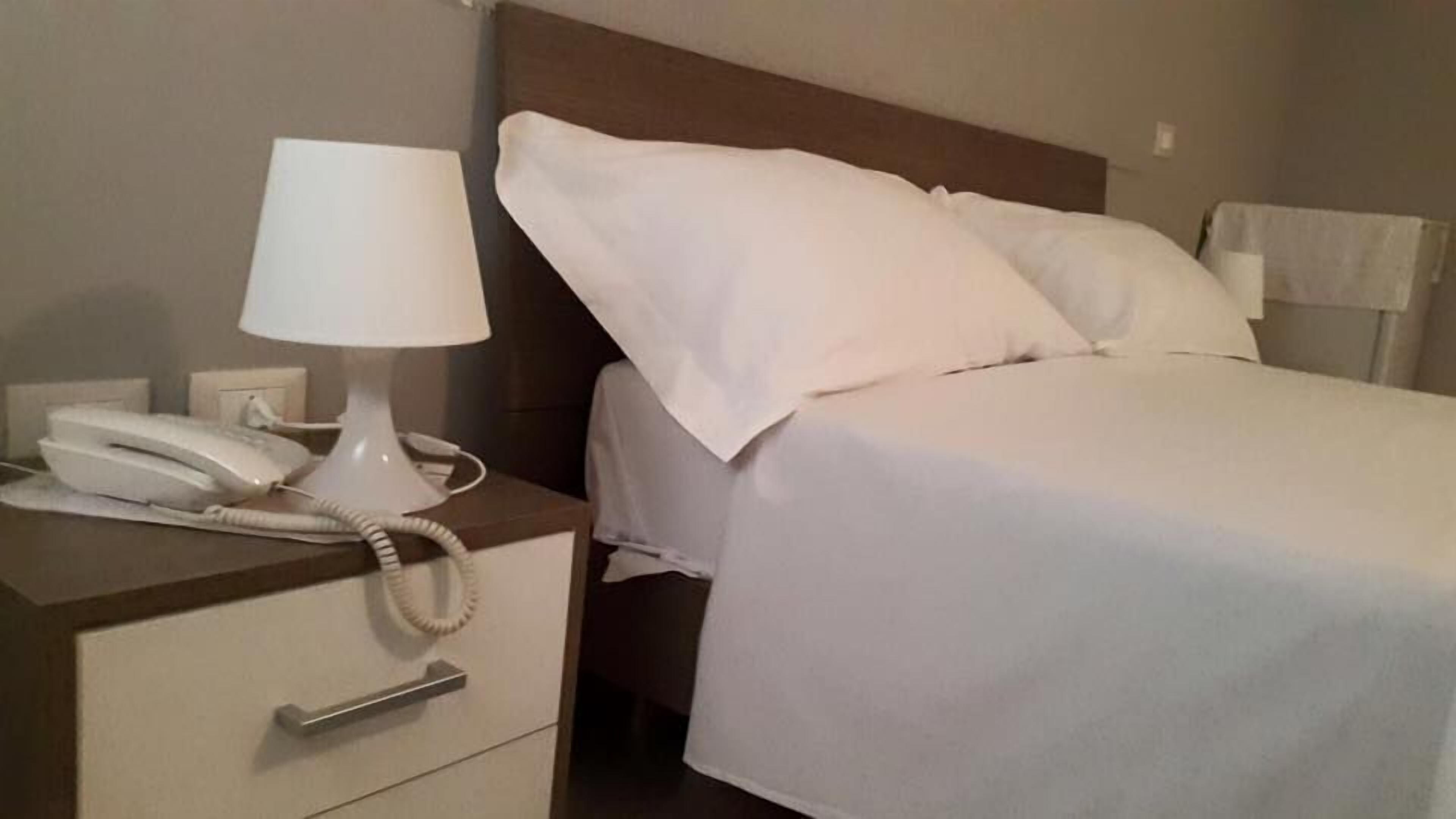 A hotel room with a bed, a nightstand, a lamp, and a telephone.