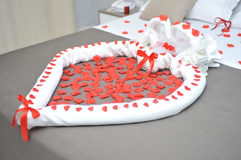 A bed with a heart-shaped bedspread and scattered rose petals.