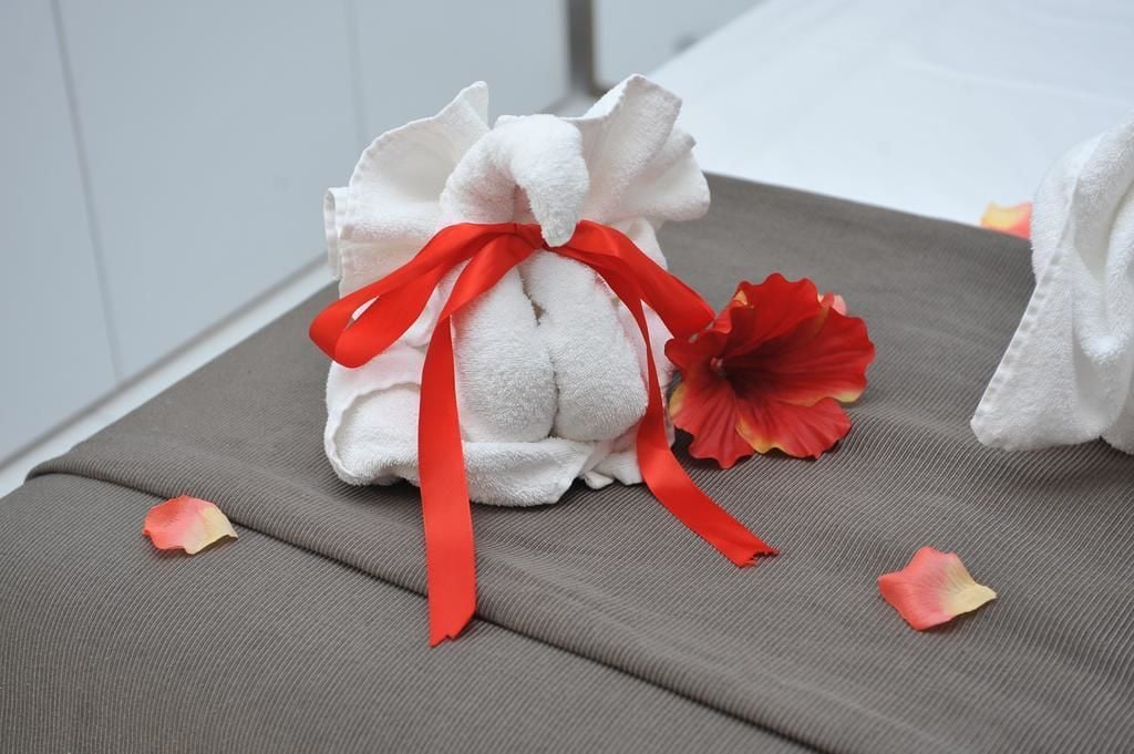 A neatly folded towel with a red ribbon tied around it, placed on a grey fabric surface.