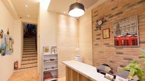 Un área de recepción con un mostrador de madera, un reloj en la pared y un cartel de una cabina telefónica roja.