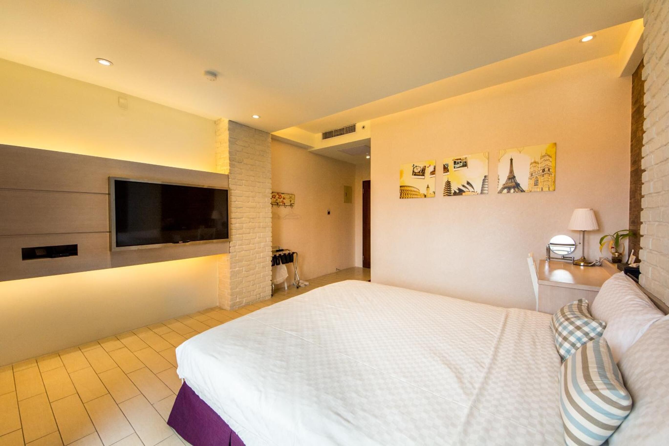 A modern hotel room with a large bed, a flat-screen TV mounted on the wall, and artwork depicting famous landmarks.