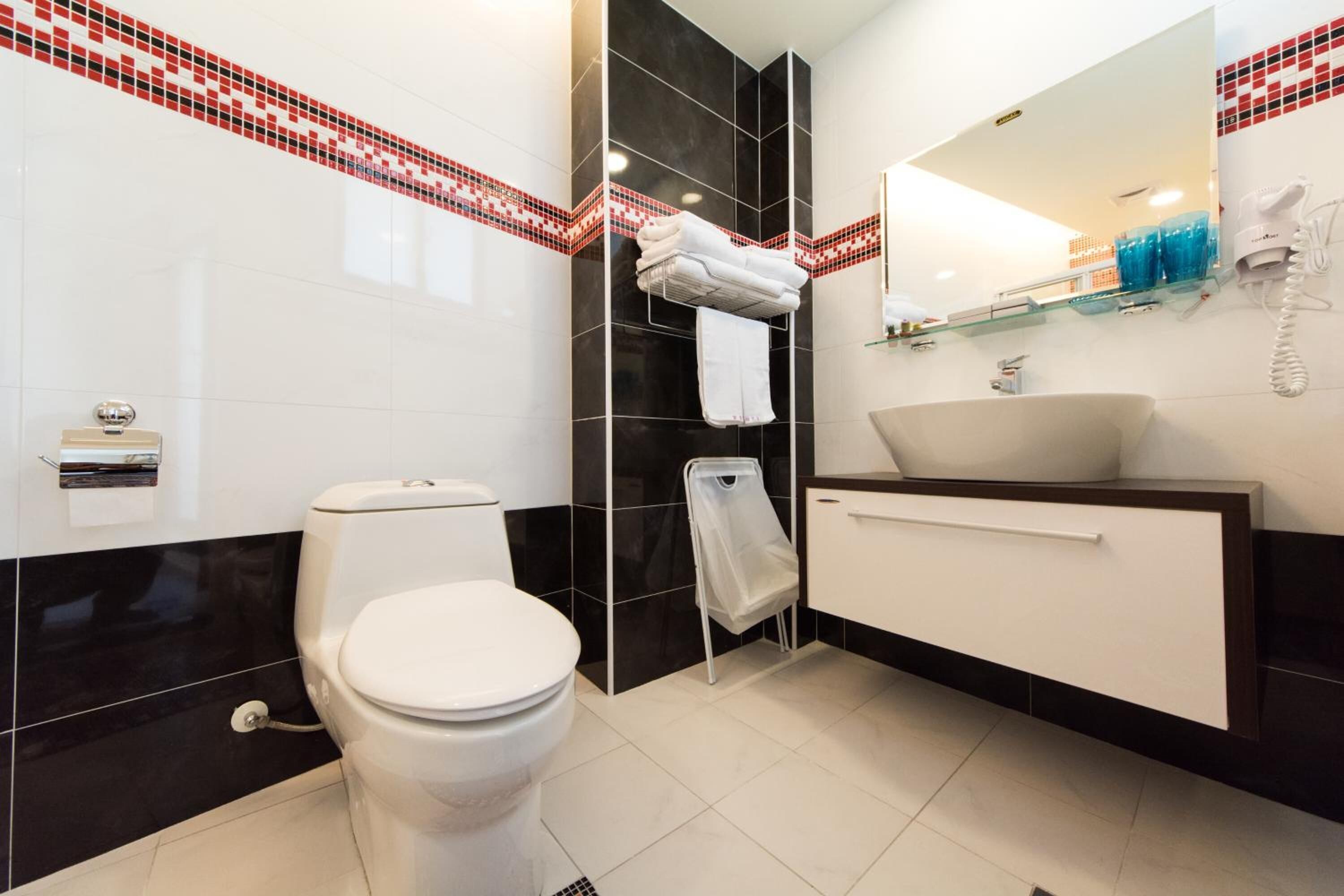 A modern bathroom with a toilet, a sink, and a mirror. There is a towel rack with folded towels and a glass shelf with toiletries.