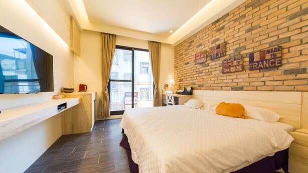 Una habitación de hotel con una cama grande, un escritorio, un televisor y una pared de ladrillo con carteles.