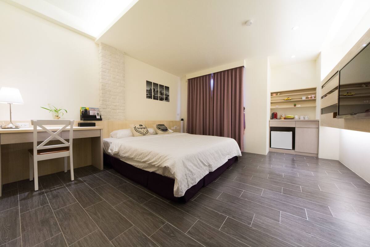Una habitación de hotel moderna con cama, escritorio, silla y kitchenette.
