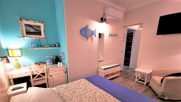 Un dormitorio con cama, escritorio, silla, espejo, estante con artículos de aseo y televisor.