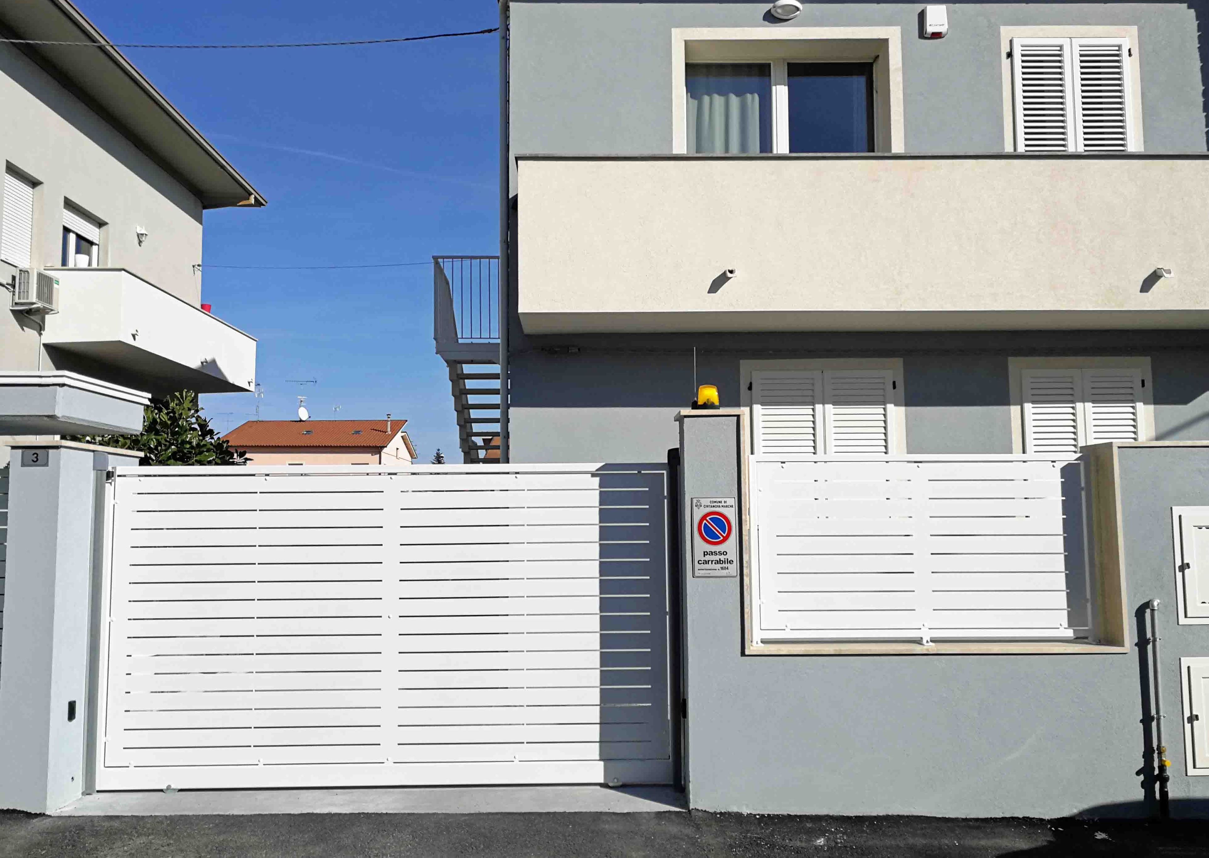 A gated residential area with a white gate, a no parking sign, and a building with a grey facade and white shutters.