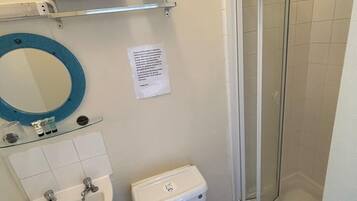 Een badkamer met een wastafel, toilet en douche. Er is een spiegel, een plank met handdoeken, en een bordje aan de muur.