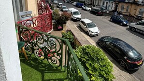 A street view with parked cars, a balcony with a green railing, and buildings with multiple stories. - The little emily - Room only (Great Yarmouth)