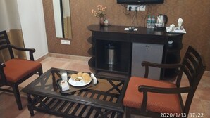 Une chambre d’hôtel dotée d’un coin repas comprenant une table avec un plateau de nourriture, deux chaises, un petit meuble, un téléviseur fixé au mur et un miroir.