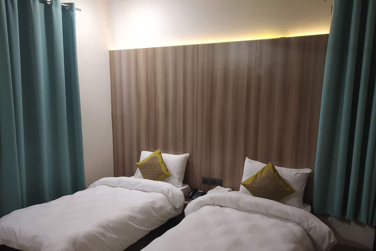 A hotel room with two single beds, a wooden headboard, teal curtains, and a bedside telephone.