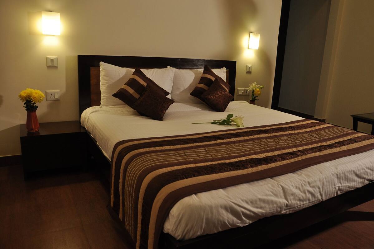 A neatly made bed with a striped bedspread, two wall-mounted lamps, and a vase with flowers on the nightstand.