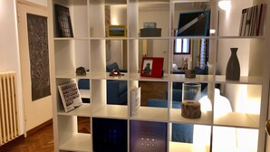A modern, well-lit room with a white shelving unit displaying various items such as books, a vase, and decorative objects. - Ca' Giulia (Venice)