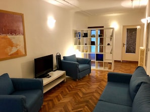 Ein Wohnzimmer mit zwei blauen Sofas, einem Fernseher und einer weißen Regaleinheit mit Dekorationen.