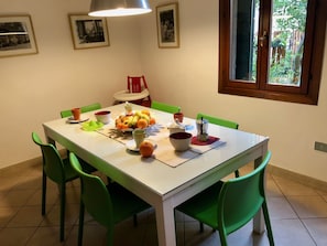Ein Essbereich mit einem weißen Tisch, grünen Stühlen und einer Obstschale.