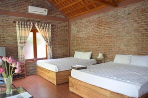 A room with two wooden beds, a brick wall, a window with curtains, and a table with a vase of flowers. - Van Long Family Homestay (Gia Vien)