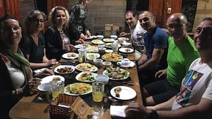 Un grupo de personas sentadas alrededor de una mesa con diversos platos y bebidas, en una habitación con paredes de madera y un ambiente rústico.