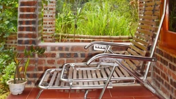 Un pilar de ladrillo, una silla de metal y una planta en maceta en un porche con vista a la vegetación.