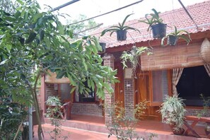 A brick building with a red-tiled roof, potted plants on the porch, and a wooden door. - Van Long Family Homestay (Gia Vien)
