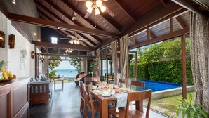 Un comedor con vista al mar, muebles de madera y una piscina al fondo.