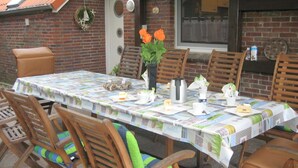 A dining area with a table covered in a patterned tablecloth, surrounded by wooden chairs with cushions. - Luxurious vacation home with a panoramic view (Bensersiel)