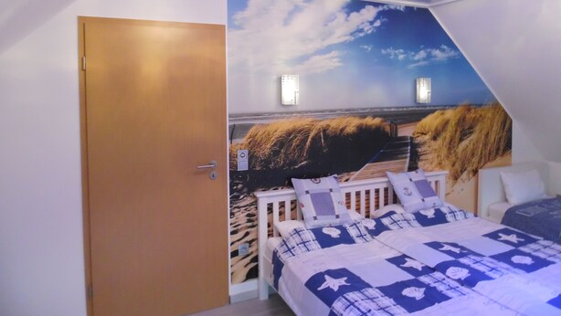 A bedroom with a mural of a beach scene, a wooden door, and a bed with a blue and white patterned bedspread. - Luxurious vacation home with a panoramic view (Bensersiel)