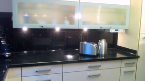 A kitchen with a black countertop, stainless steel toaster, and kettle. There are white cabinets with silver handles and a white backsplash. - Luxurious vacation home with a panoramic view (Bensersiel)