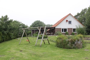 Een huis met een rood dak en een bakstenen gevel. Voor het huis staat een schommel en een houten ladder leunt tegen een constructie.