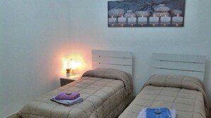 A bedroom with two beds, each with a beige duvet and pillows, a nightstand with a lamp, and a wall-mounted picture of candles. - Bed and Breakfast Ocurniciell (Naples)