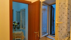 A room with a wooden door leading to a dining area with a table and chairs, a window with a patterned curtain, and a view of the outside. - Bed and Breakfast Ocurniciell (Naples)