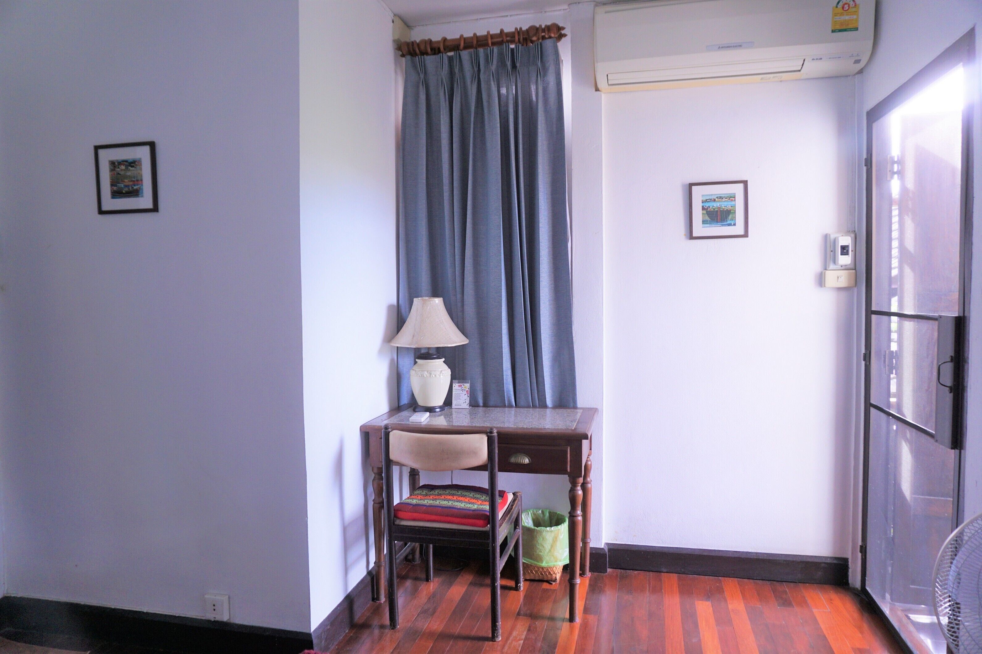 A room with a desk, chair, lamp, and a waste bin.