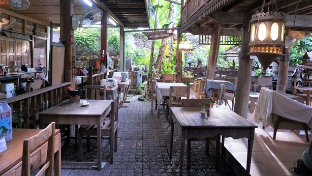 Un restaurante al aire libre con mesas y sillas de madera, rodeado de abundante vegetación.