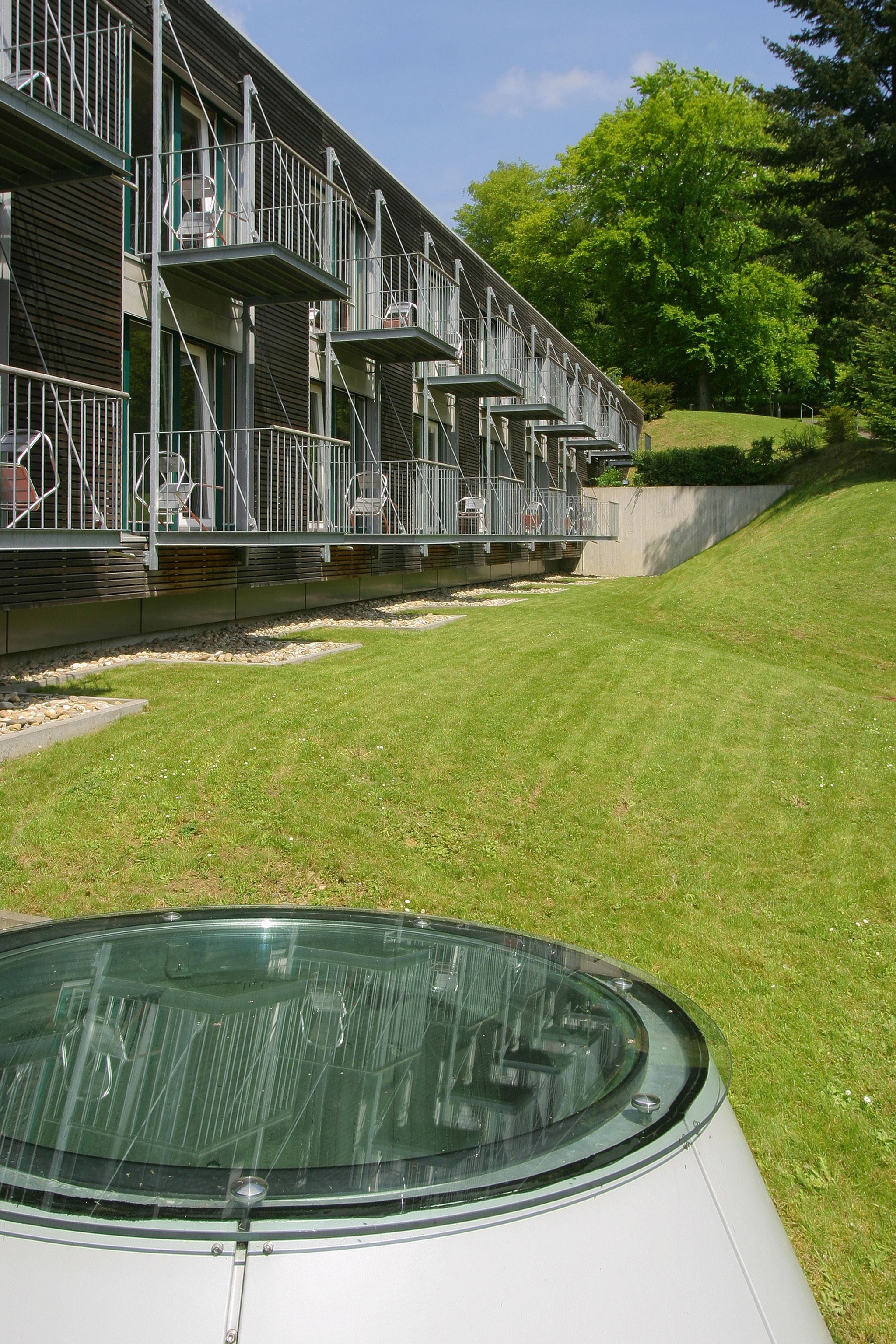 A modern building with multiple balconies and a grassy area in front.
