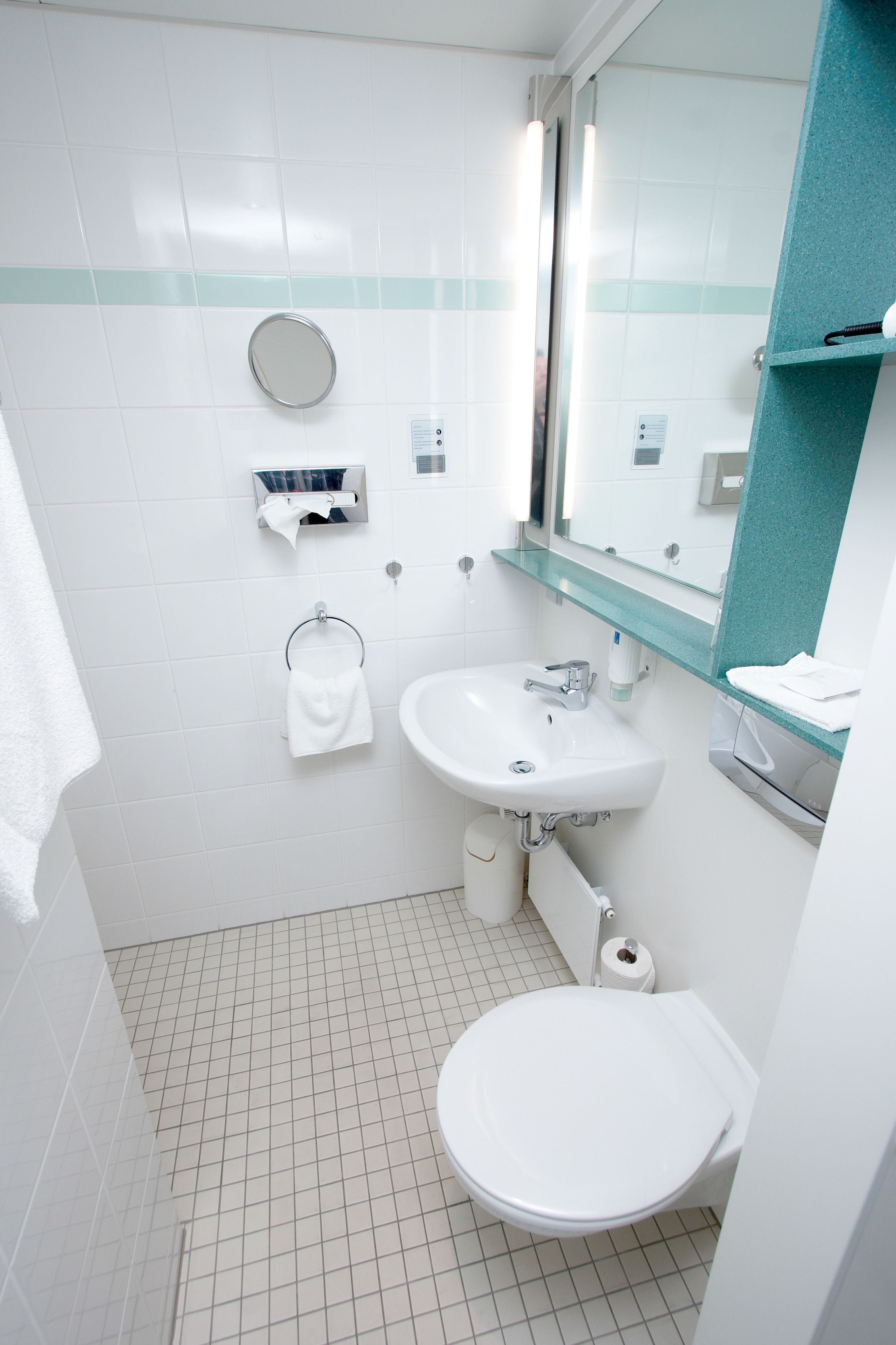 A bathroom with a toilet, sink, and mirror. There is a towel rack and a soap dispenser on the wall.