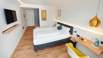 Une chambre d’hôtel moderne avec un grand lit, un bureau avec une chaise, une télévision et une salle de bain avec une chaise jaune.