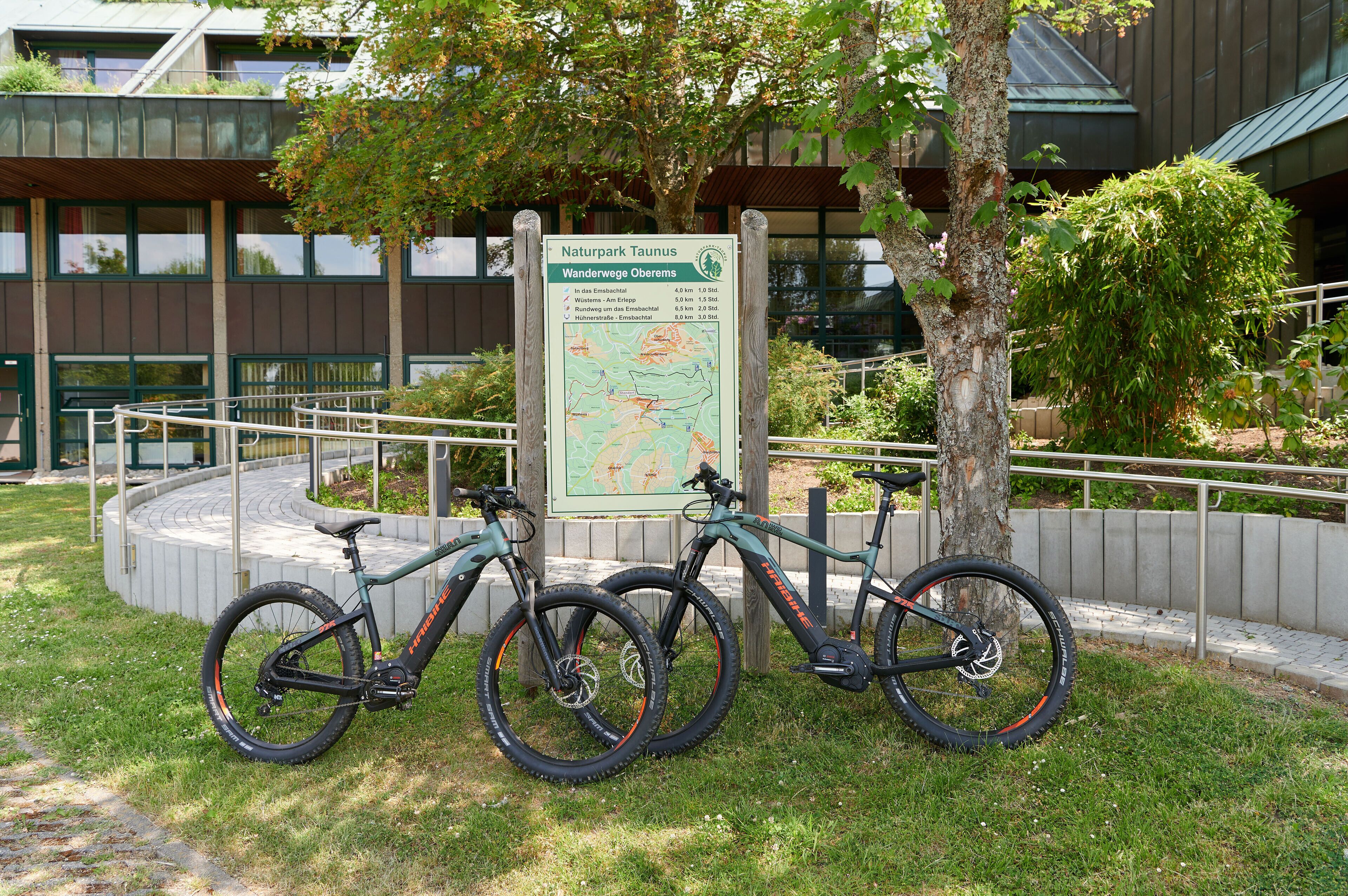 Una bicicleta apoyada en un cartel en un área ajardinada, con un edificio al fondo.