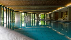 Une piscine intérieure avec des parois en verre transparent, un sol carrelé et des chaises longues disposées le long des côtés.