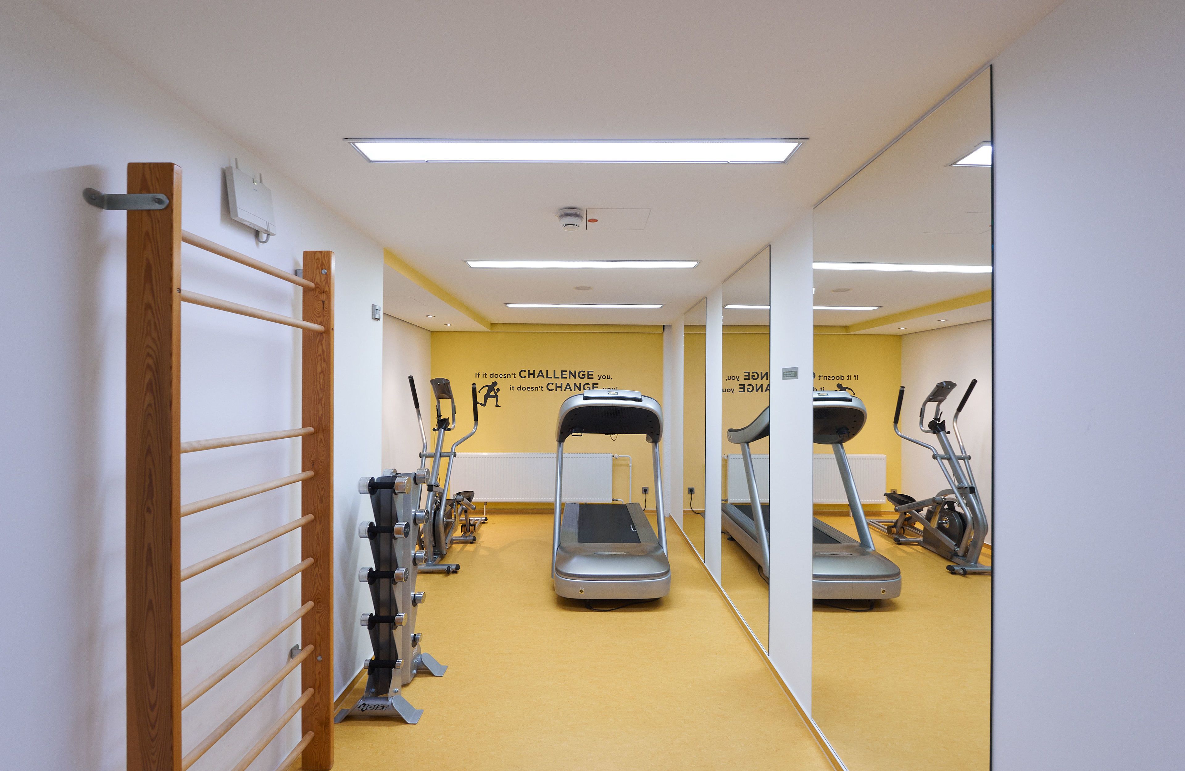 Ein Fitnessraum mit Trainingsgeräten, einem Spiegel und motivierenden Sprüchen an der Wand.