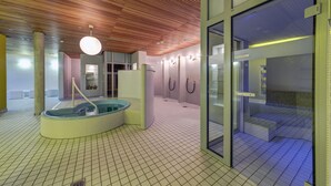 Un spa moderne doté d’un plafond en bois, d’une grande porte vitrée et d’un jacuzzi circulaire.