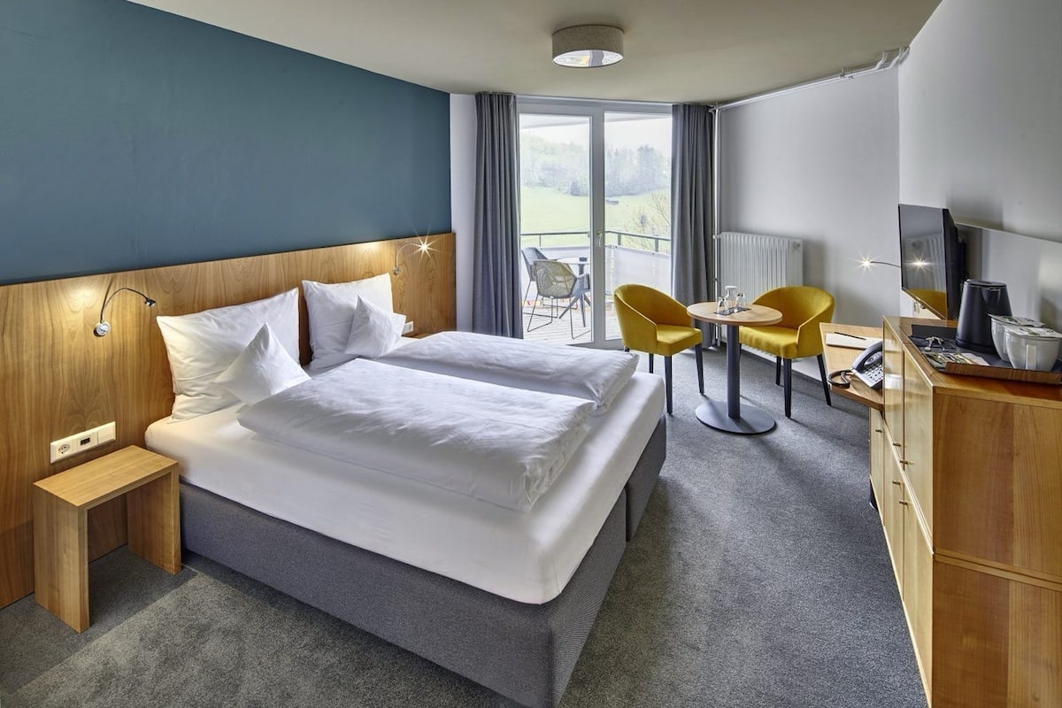 Une chambre d’hôtel avec un grand lit, deux tables de chevet, un bureau avec une chaise, une petite table avec deux chaises et un téléviseur.